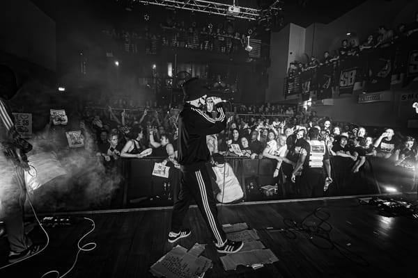 B&W photo of The Skinner Brothers singer on stage at Scala with the camera facing the audience. Fans in the crowd hold "WE ❤️ THE SB" signs.